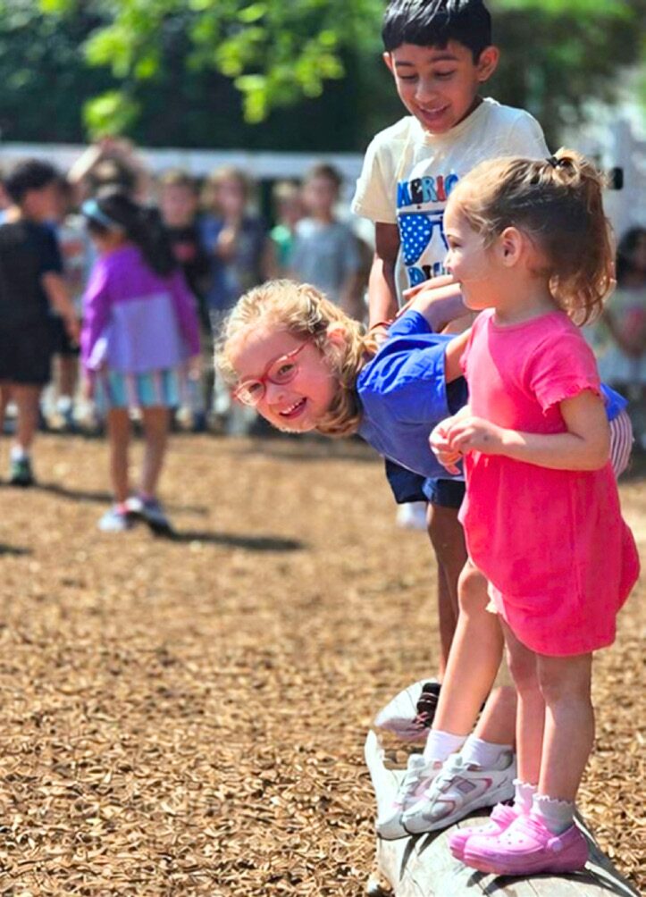 A student in a pink dress plays on the playground with classmates around her.